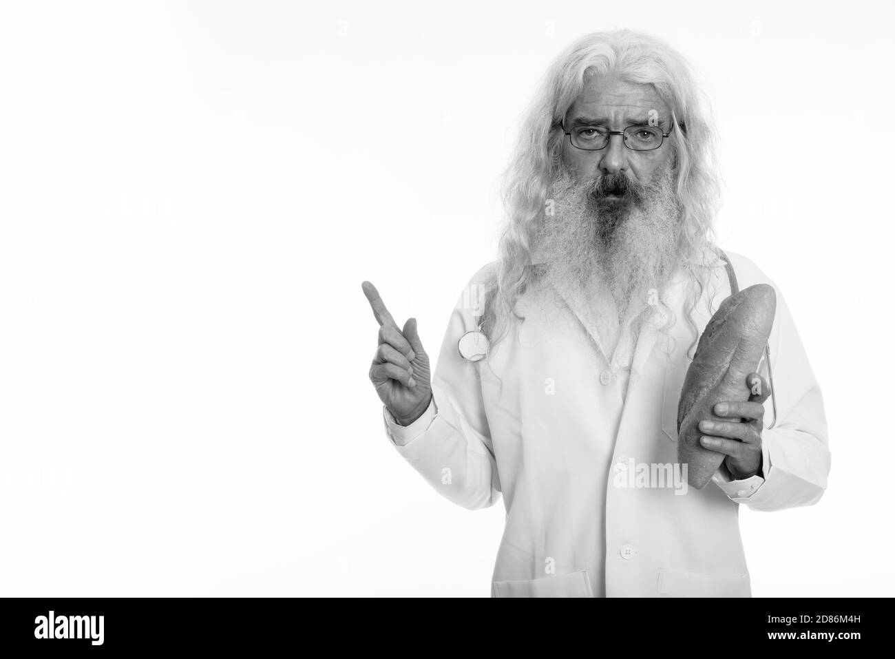 Studio shot di senior uomo barbuto medico indossando occhiali tenendo premuto il pane e puntare il dito fino Foto Stock