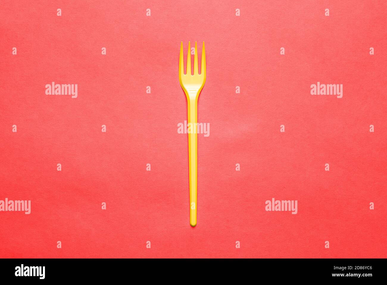 Forcella di plastica gialla su sfondo rosso. Posate monouso per mangiare. Stoviglie. Stile minimalista e creativo Foto Stock