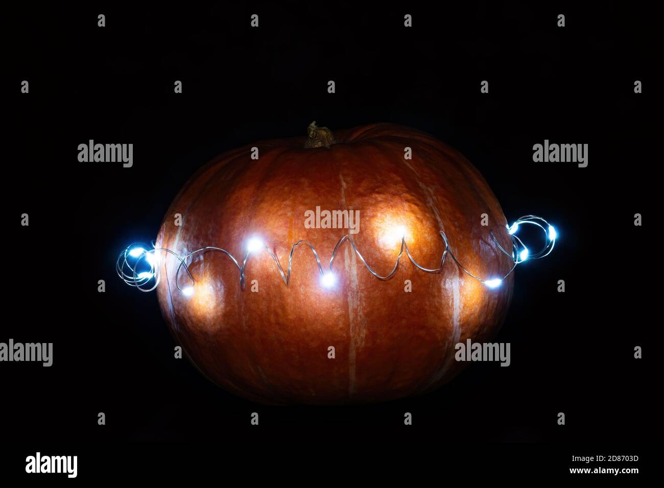 Zucca arancione avvolta in una ghirlanda ardente al buio. Giorno di ringraziamento e concetto di Halloween Foto Stock