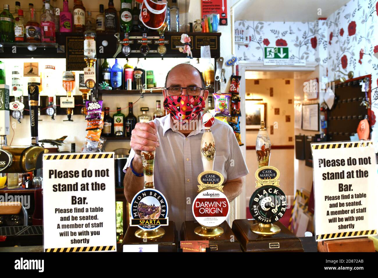 Llanymynech il villaggio che si trova a cavallo tra Inghilterra e Galles. Bob Hedley il padrone di casa dei Bradford Arms a Llanymynech dietro il suo bar che indossa un volto ma Foto Stock