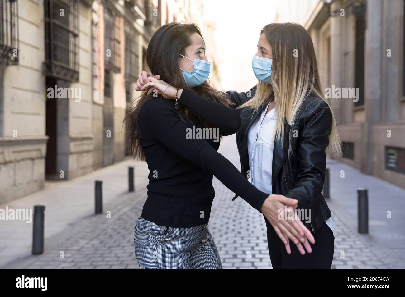 Due ragazze che ballano in mezzo alla strada. Indossano una maschera facciale. Concetto di nuova normalità. Foto Stock