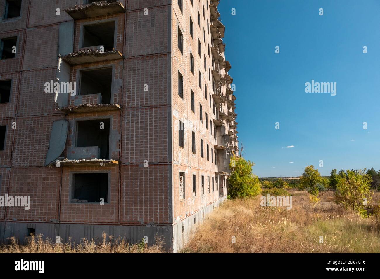Alto edificio sovietico abbandonato a più piani con facciata piastrellata rossa sul paesaggio soleggiato autunnale. Città incompiuta di scienziati nucleari a Birky, Ucraina Foto Stock