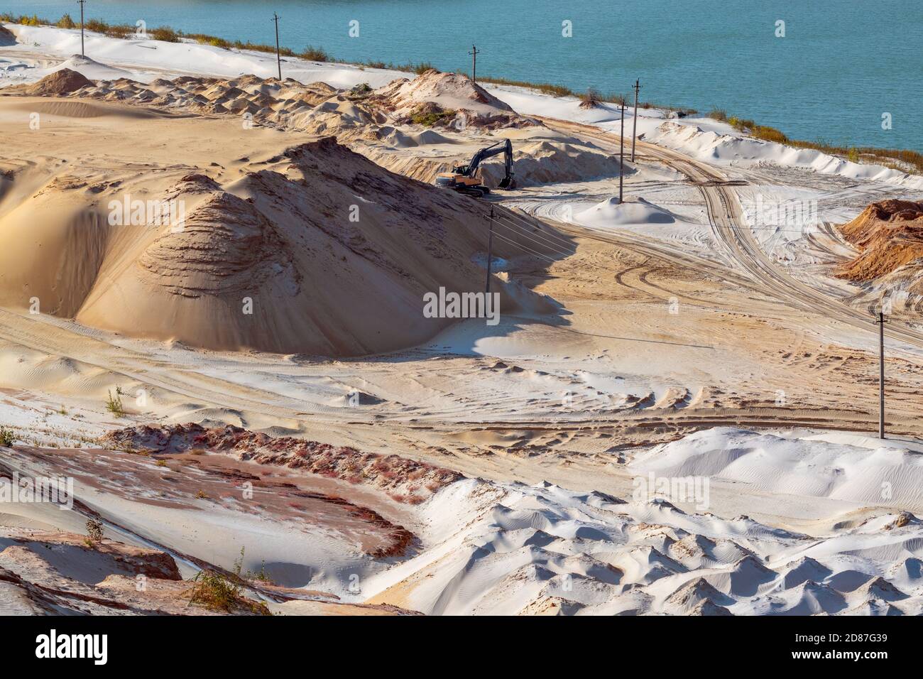 Estrazione della sabbia con macchina scavatrice in cava di quarzo. Dune di sabbia colline terreno scavare vicino lago Foto Stock