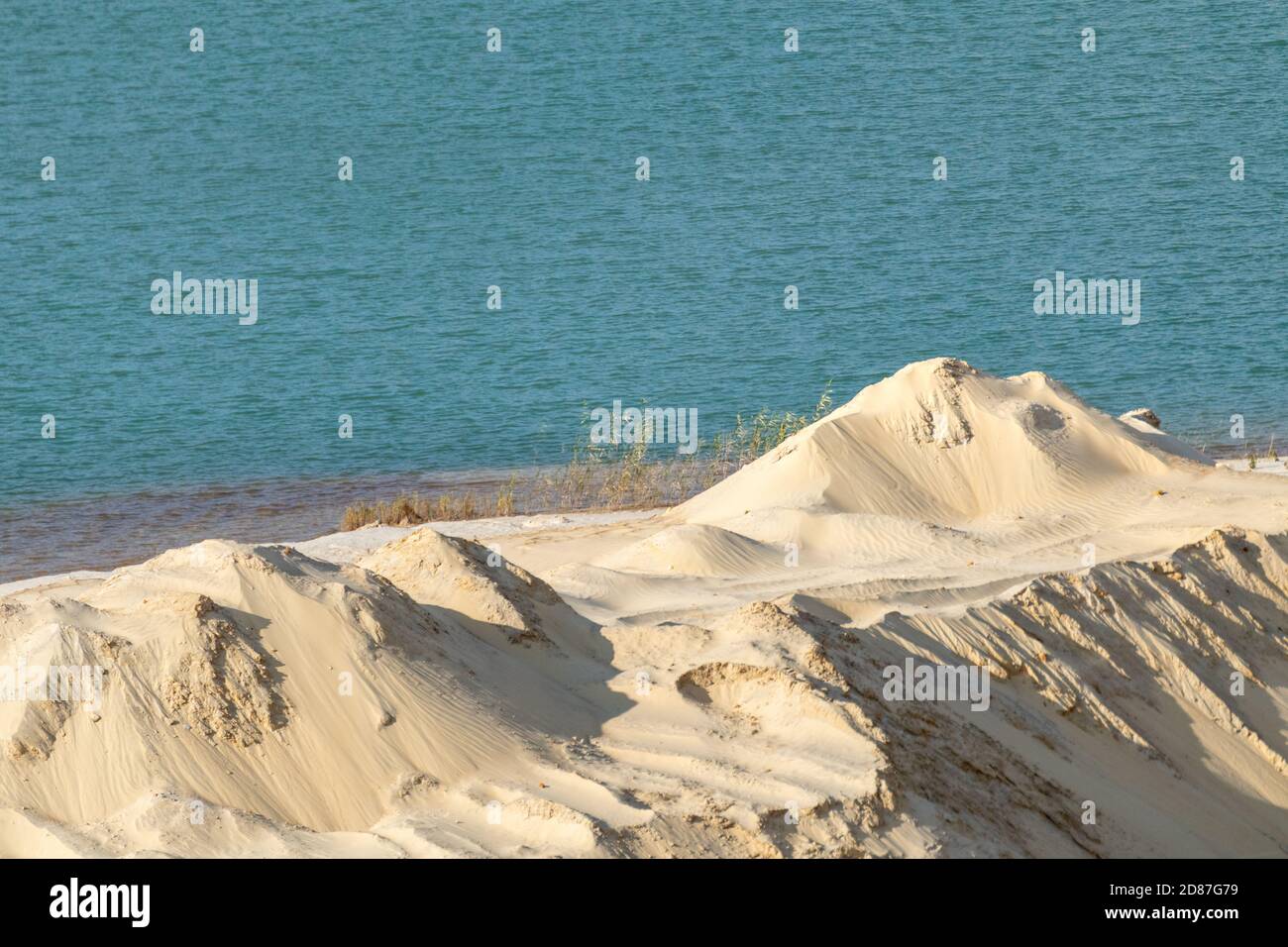 Dune di sabbia gialla e terreno desertico naturale di acque blu. Motivo ondulato di sabbia di cava Foto Stock