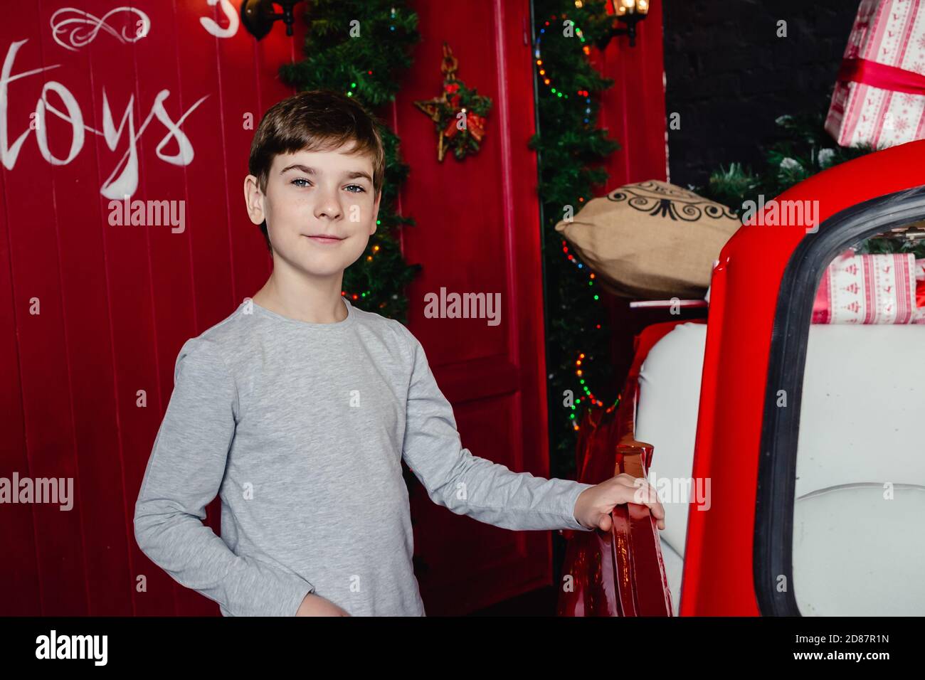 Adorabile ragazzo sorridente e sicuro con sorriso sul viso vicino decorazione di natale e un sacco di regali a casa. Umore di Natale. Vacanze. Foto Stock