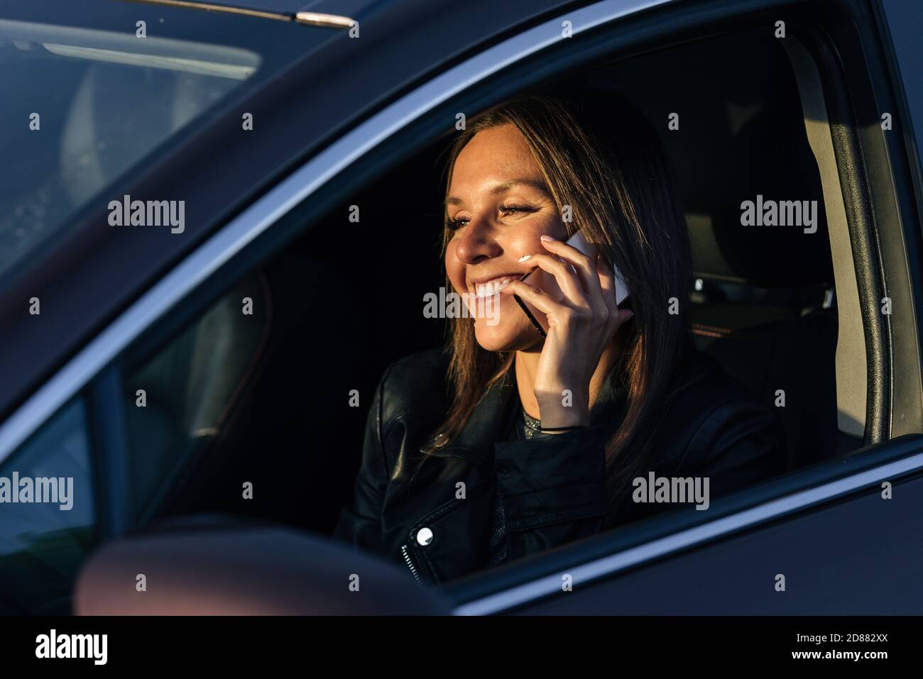 Felice donna sorridente che parla al telefono mentre guida un auto in una giornata di sole Foto Stock