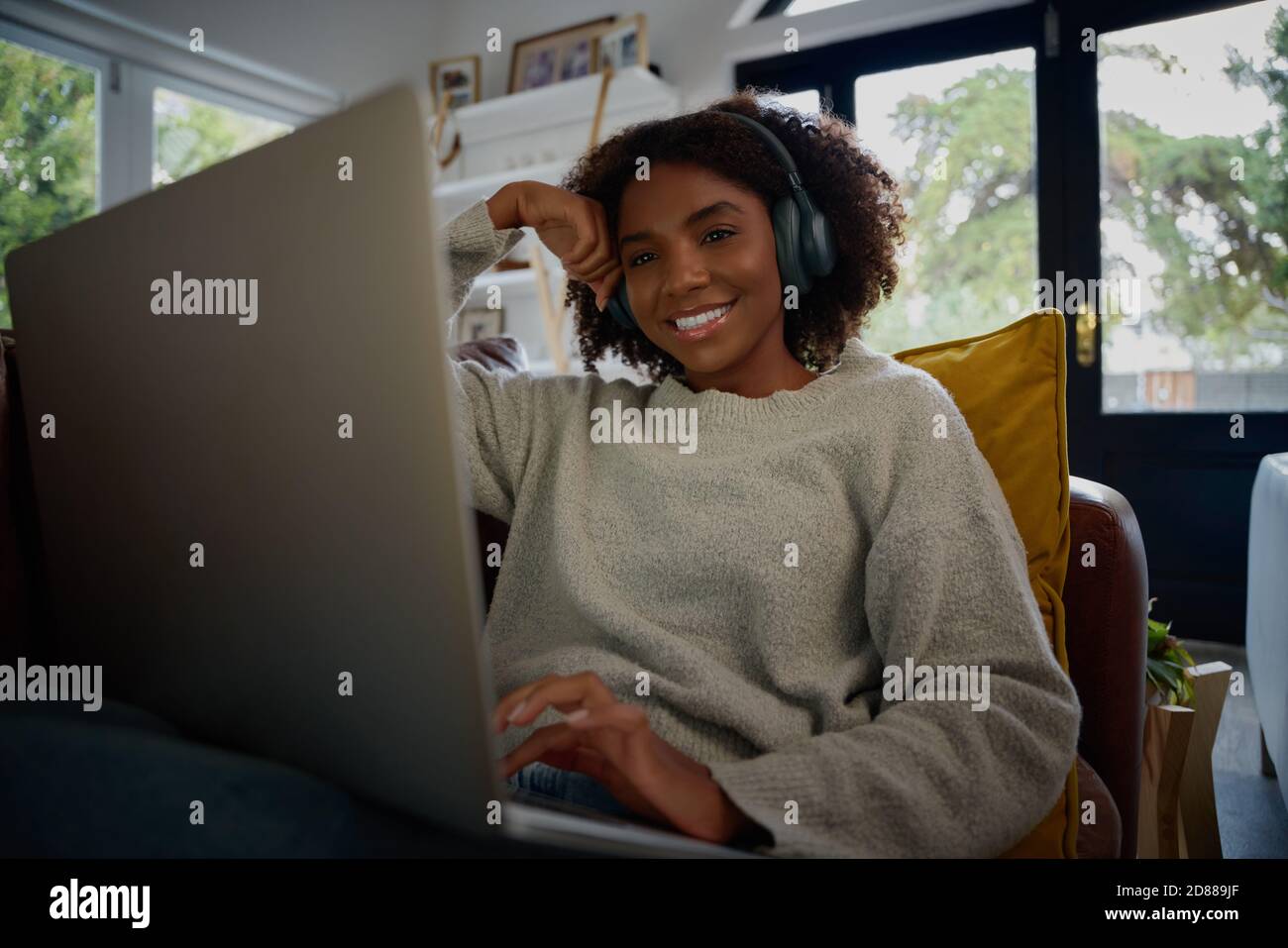 Ritratto di giovane donna nera allegra che ascolta l'audio in cuffie durante la visione di video sul computer portatile a casa Foto Stock