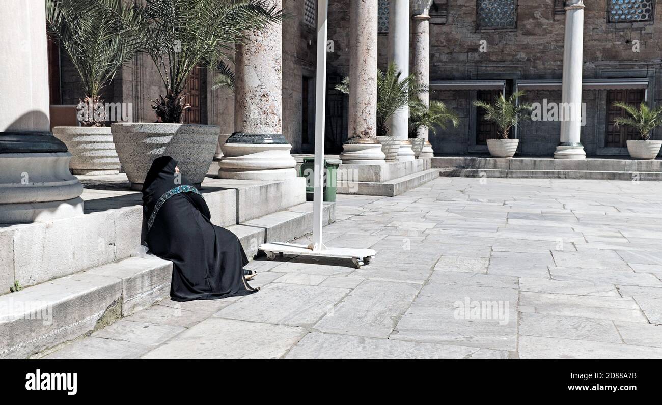 Una donna turca più anziana vestita nel tradizionale hijab nero si trova da sola in un cortile a Istanbul, Turchia. Foto Stock
