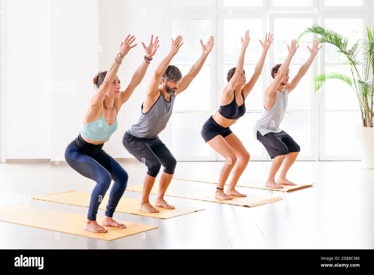 Gruppo di persone che fanno Utkatasana o sedia posa mentre si pratica yoga nella luminosa e spaziosa palestra Foto Stock