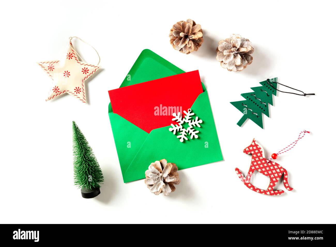 Un biglietto d'auguri di Natale rosso in una busta verde, girato dall'alto su uno sfondo bianco con decorazioni per il nuovo anno e un luogo per il testo Foto Stock