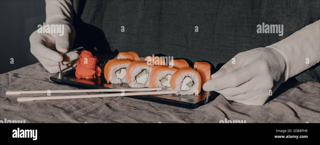 Le mani in guanti di gomma servono il sushi su un supporto nero. Menu sushi. Foto Stock