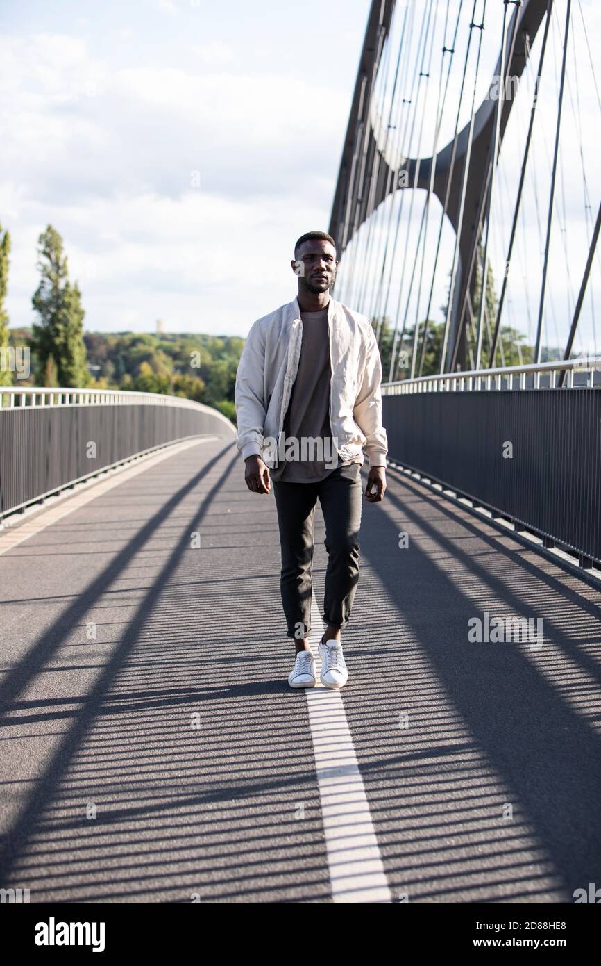 Bell'uomo nero che cammina sul ponte pedonale con sicurezza. Lunghezza completa. Verticale. Foto Stock