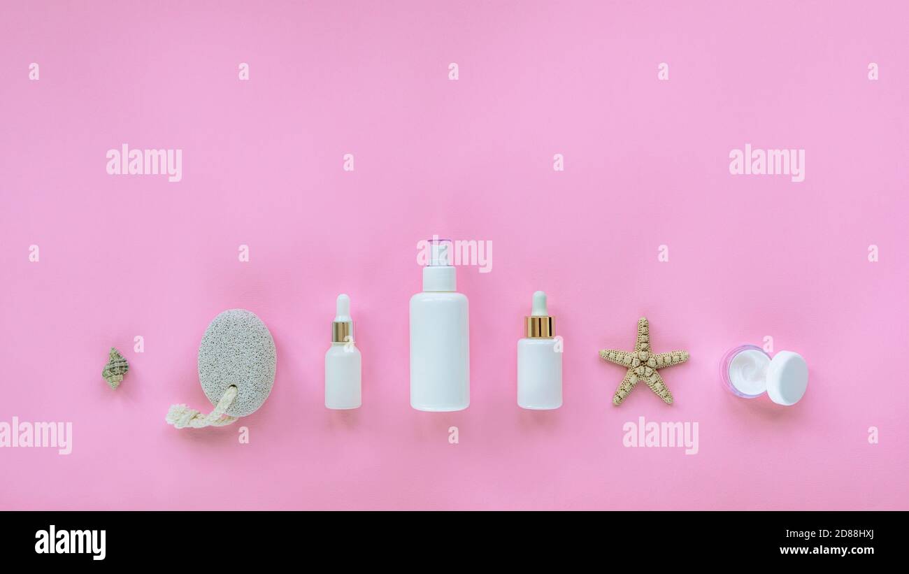 Prodotti naturali biologici per la cura della pelle. Siero, vasetto per crema, tonico, olio cosmetico in bottiglie bianche senza marchio, pietra pomice, conchiglia. Sfondo rosa, t Foto Stock