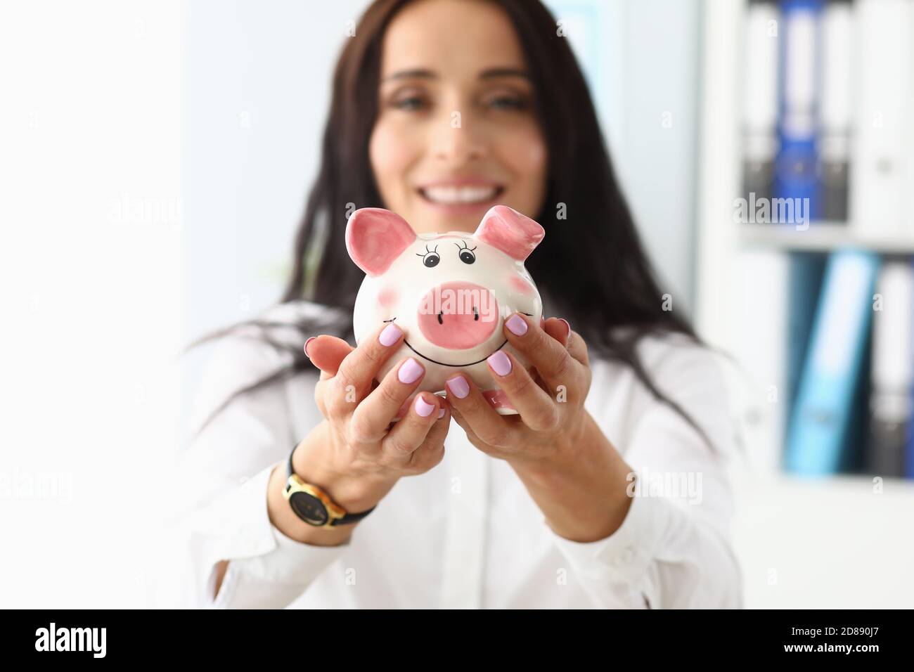 Giovane bella donna che tiene la banca del piggy in forma di maiale nelle mani in primo piano Foto Stock