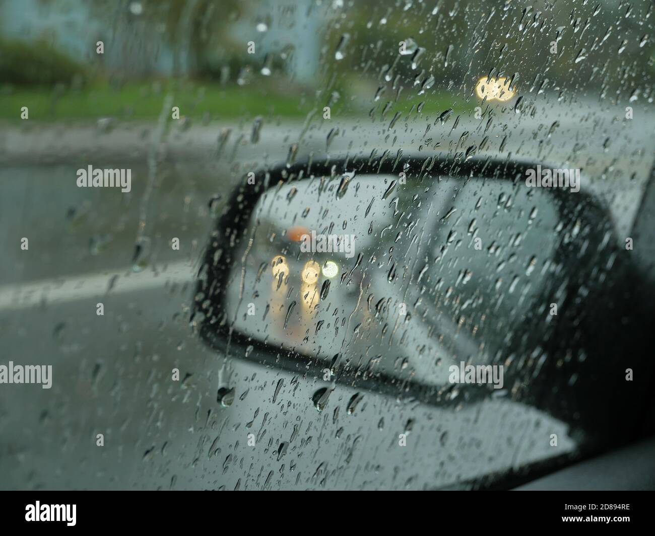 lo specchietto retrovisore dell'auto si trova su una strada piovosa che passa Foto Stock