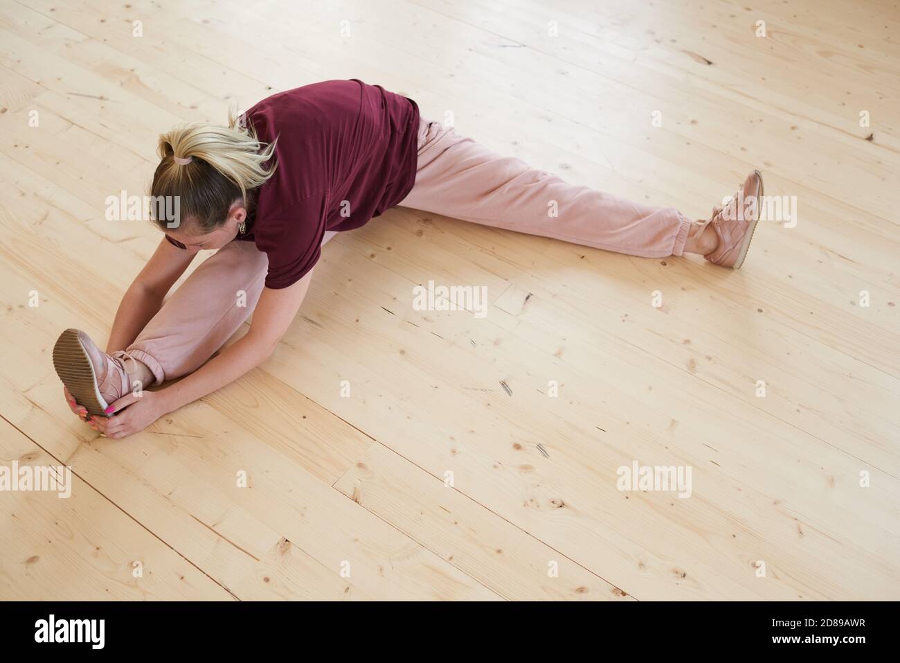 Giovane donna sana seduta sul pavimento e in riscaldamento prima di allenamento sportivo nel centro benessere Foto Stock