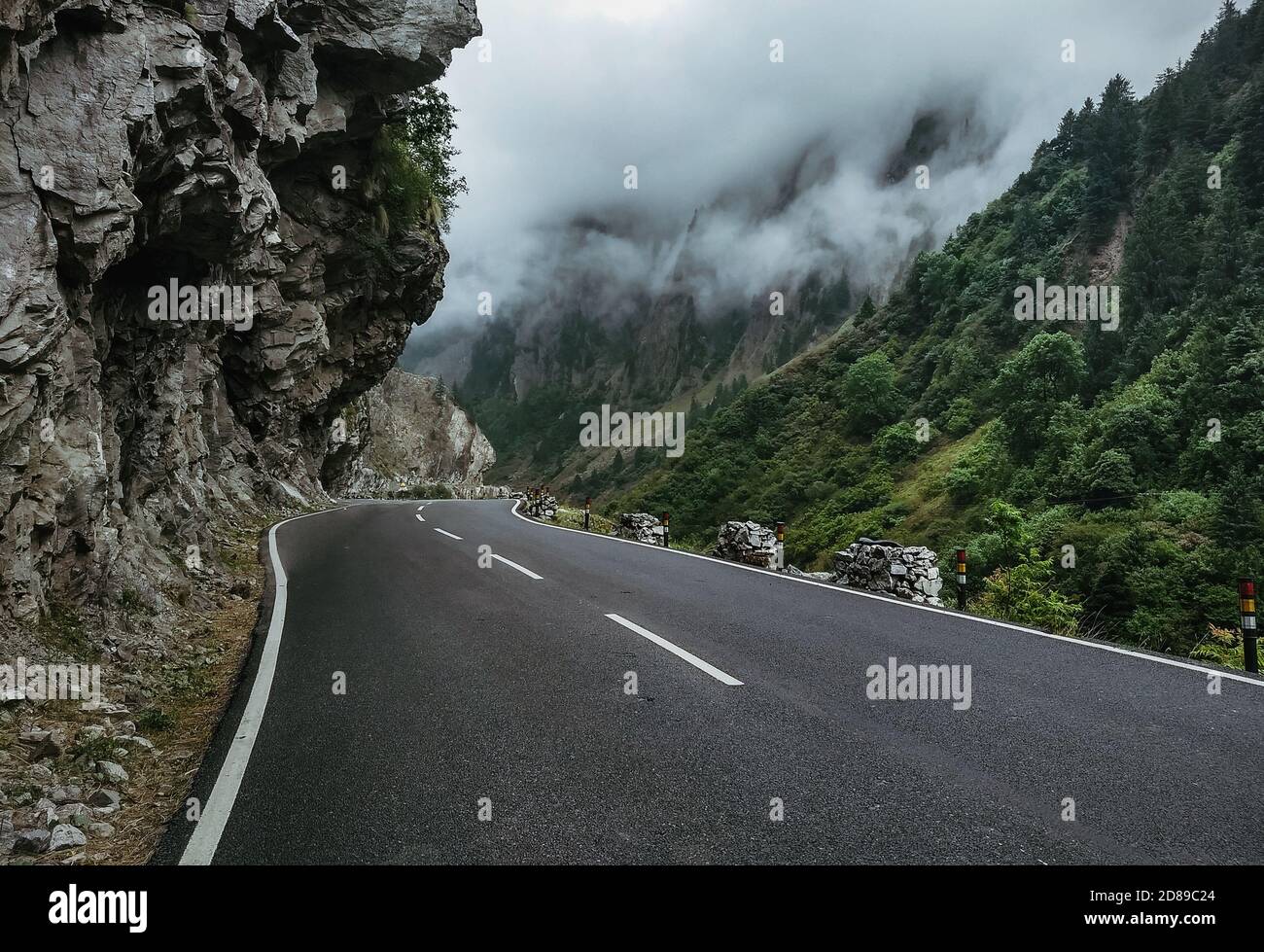 Una strada vuota con montagne verdi e nuvole vicino al laterale Foto Stock