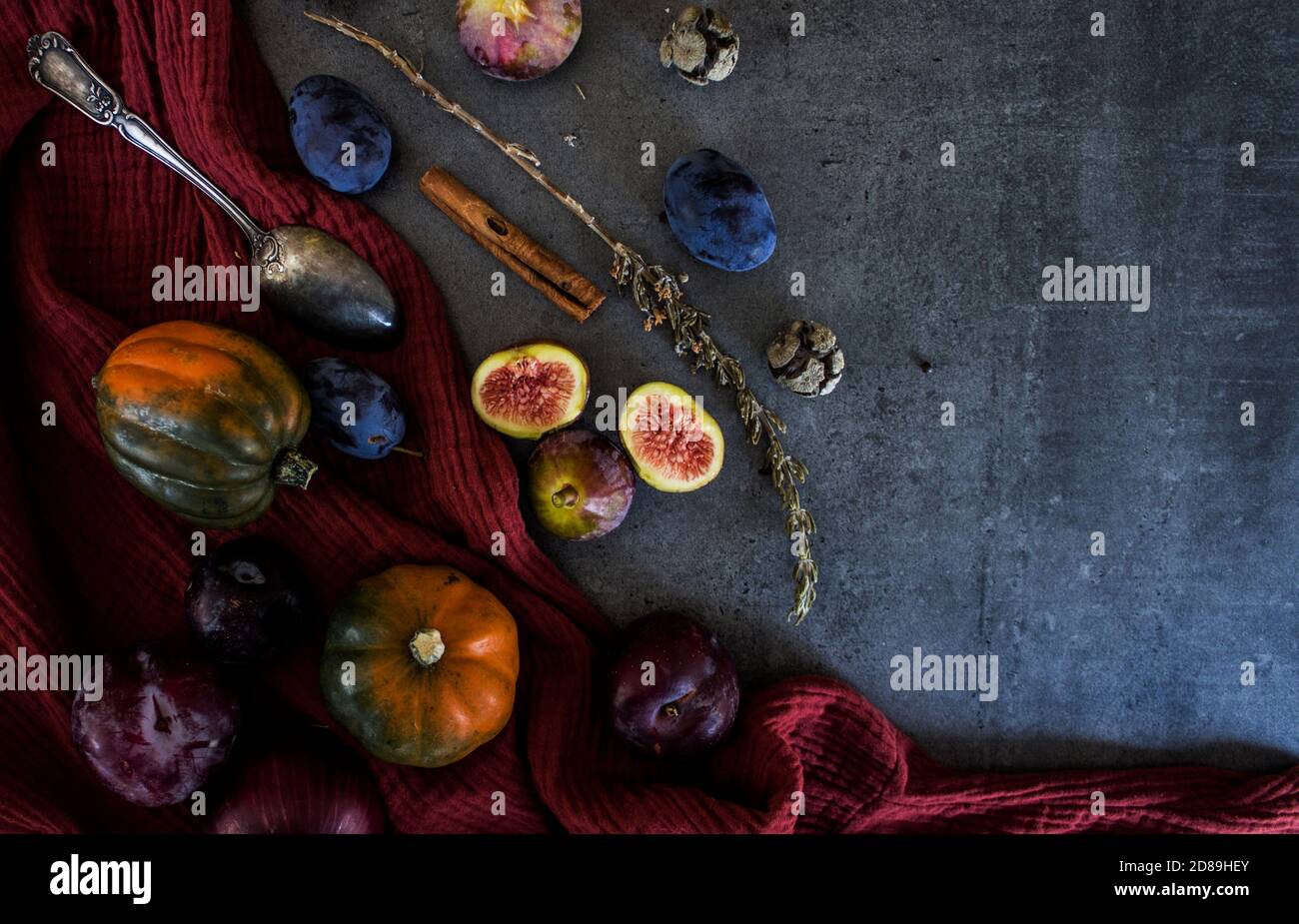 Frutta fresca e verdure su un tavolo. Zucca gemma, prugne, fichi e cucchiaio d'argento su sfondo grigio. Vista dall'alto della vendemmia autunnale. Foto Stock