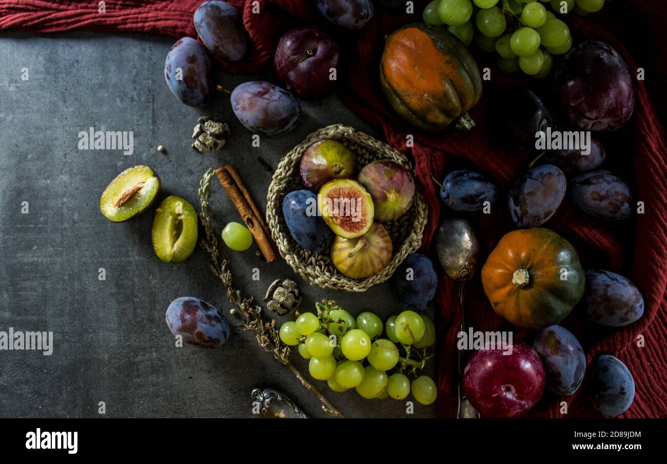 Ancora vita con frutta fresca e verdure su tavola grigio scuro. Foto dall'alto di squadroni di gemme, uva, prugne, asciugamano da cucina rosso testurizzato. Foto Stock