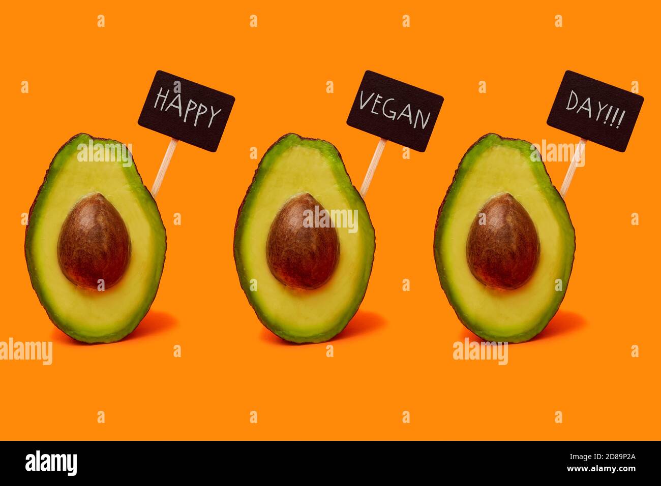 frutta di avocado dimezzata su sfondo arancione con nero segni che leggono felice giorno vegano Foto Stock