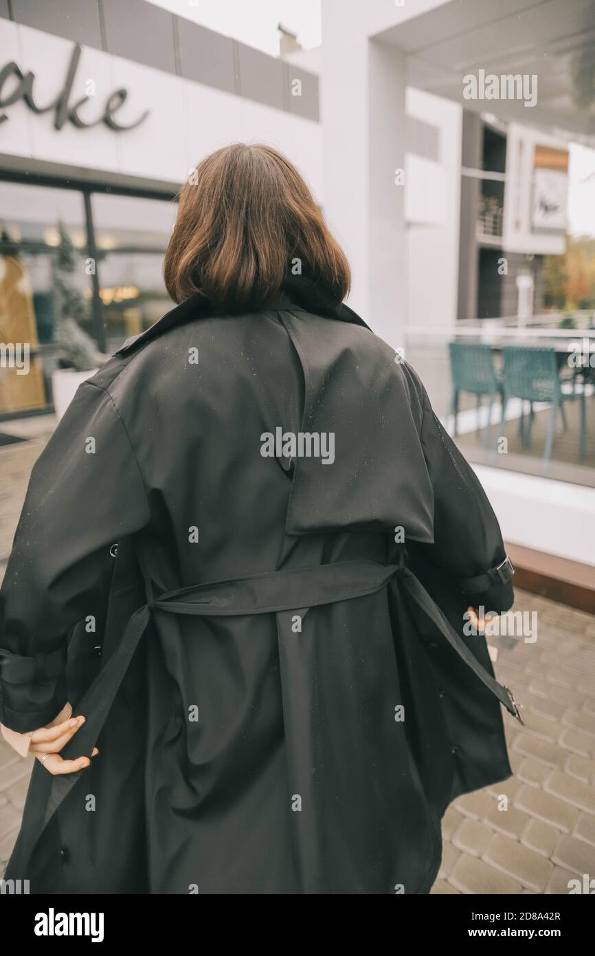ragazza alla moda in un cappotto sta camminando sotto la pioggia in fondo  alla strada Foto stock - Alamy
