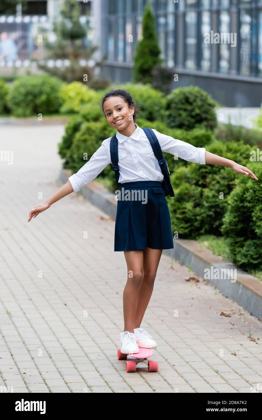 felice aloafroamericana studentessa con zaino cavalcare penny bordo all'aperto Foto Stock