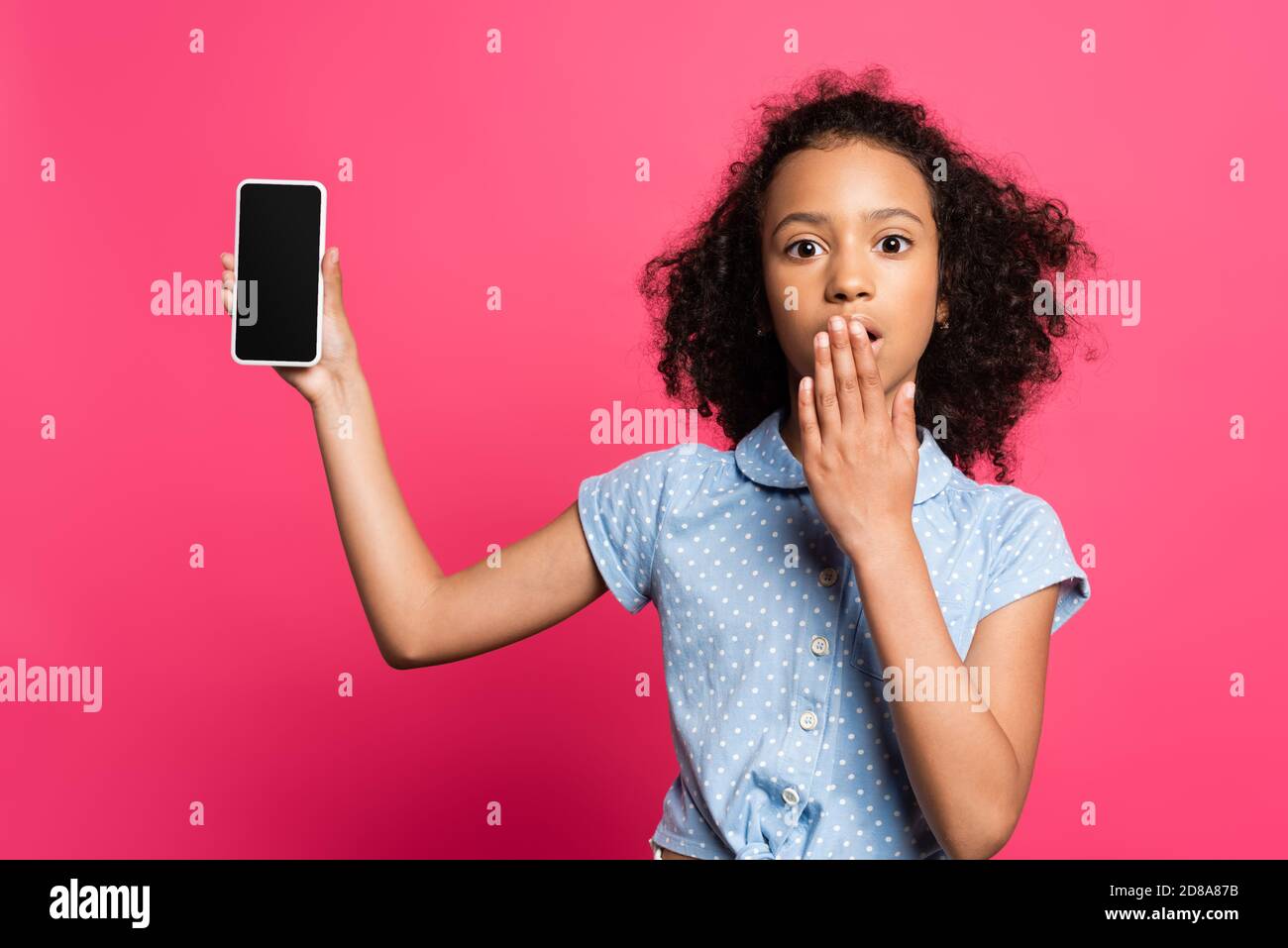 scioccato capretto afro-americano che presenta smartphone isolato su rosa Foto Stock
