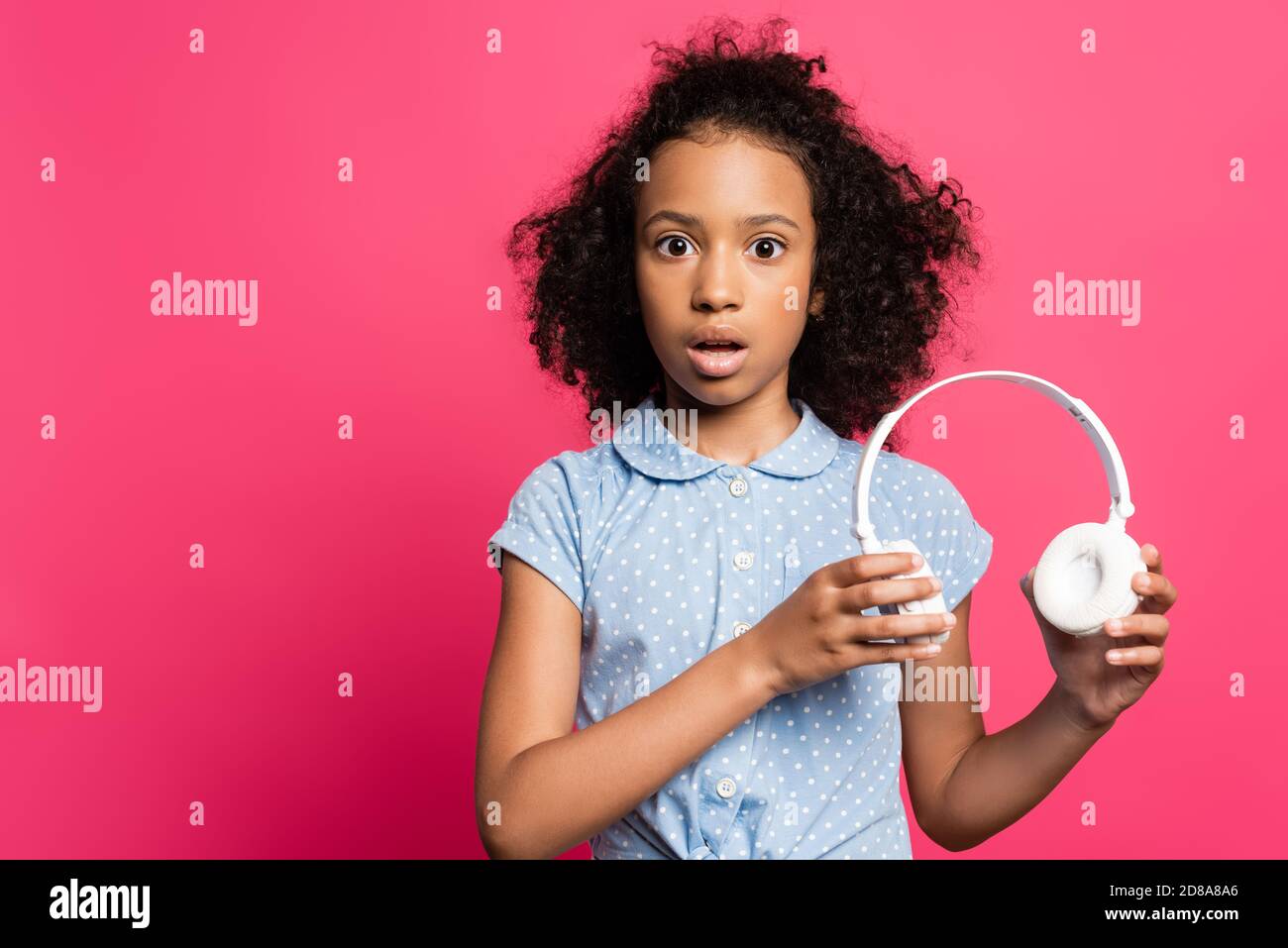 scioccato carino ricciolo afroamericano con le cuffie isolate rosa Foto Stock