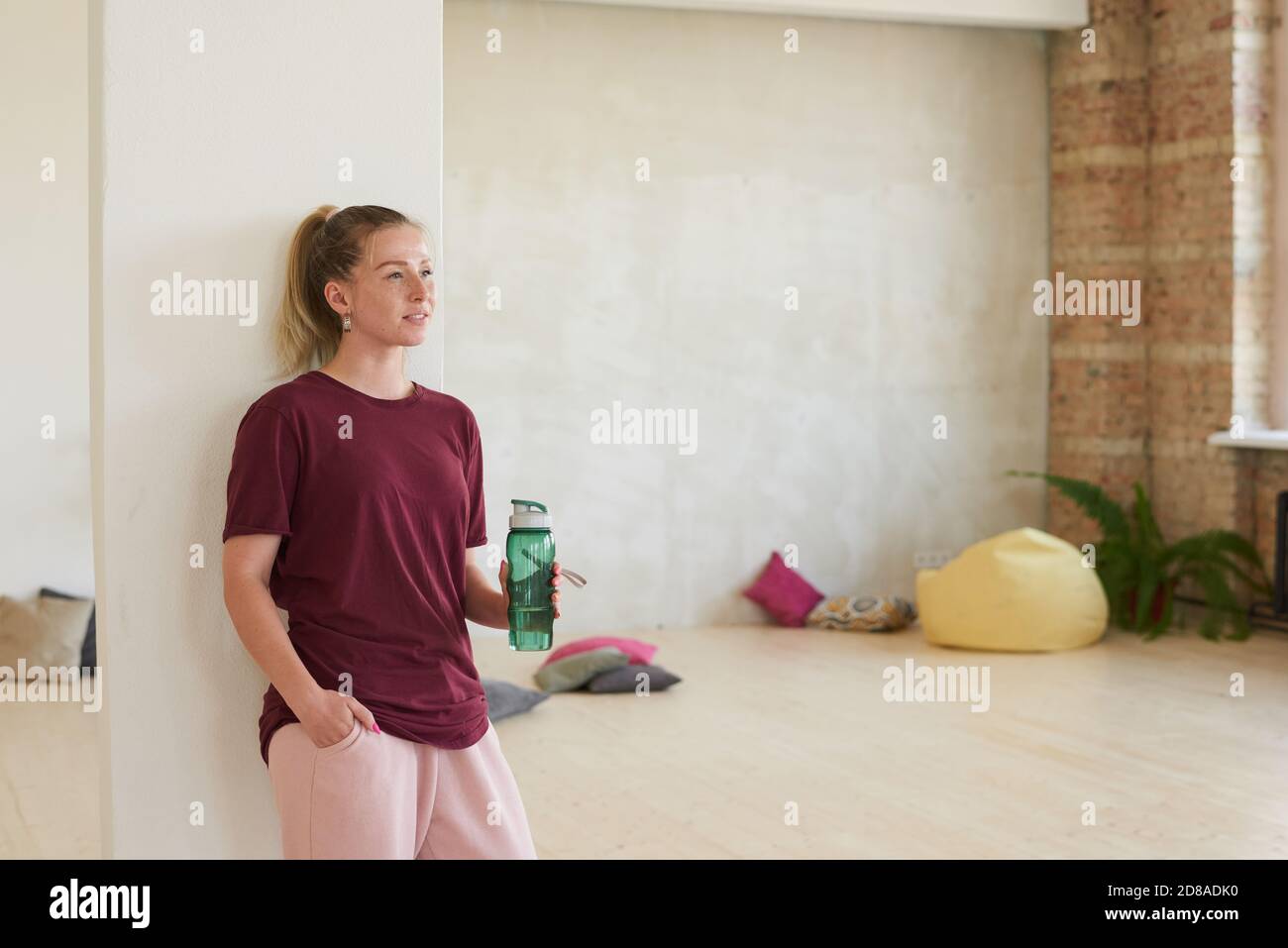 Giovane donna in abbigliamento sportivo in piedi in studio di danza con bottiglia d'acqua che riposa dopo l'allenamento Foto Stock
