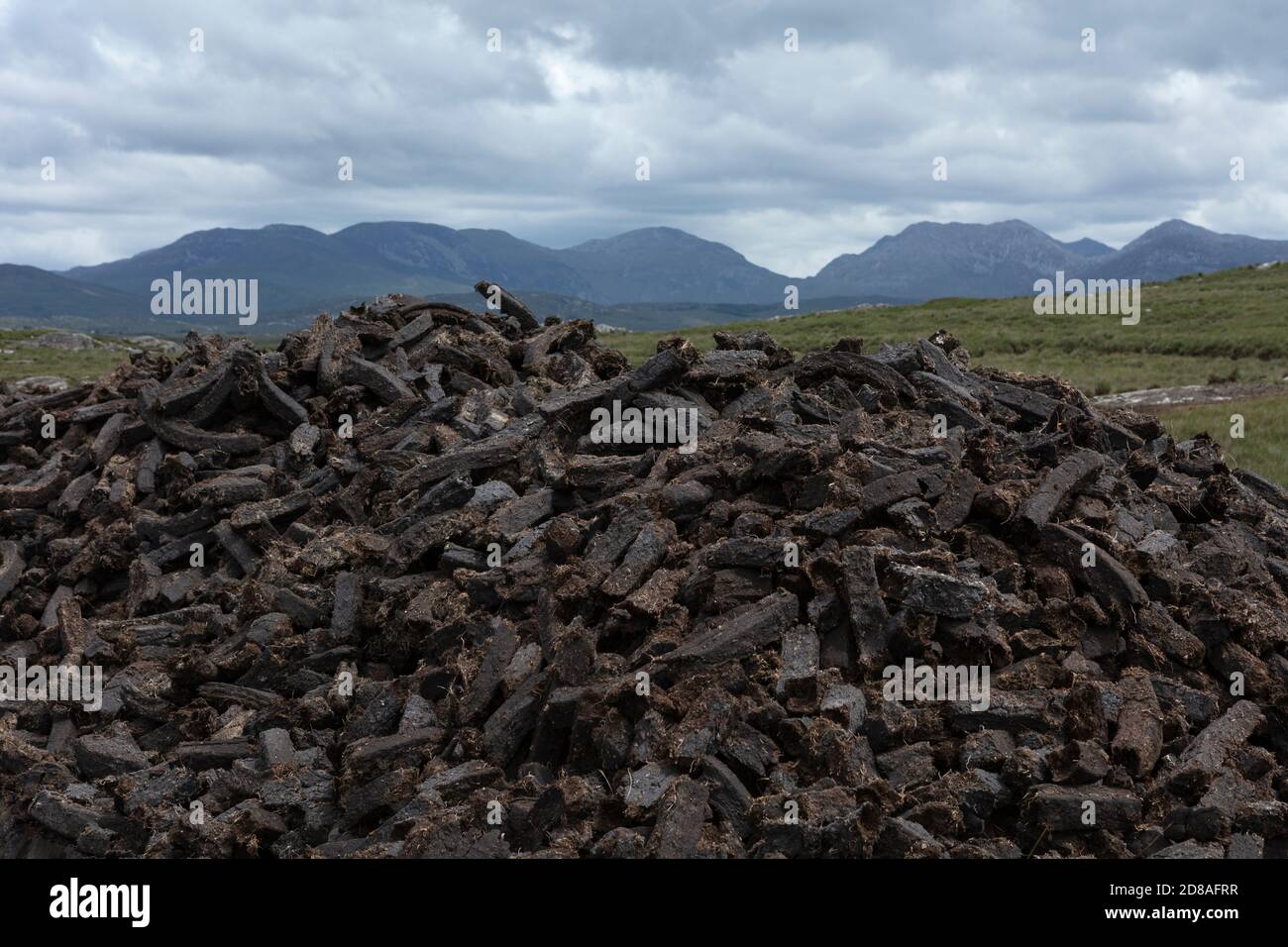 Taglio di torba (torba) a Connemara, Galway, Irlanda, con le montagne del Connemara sullo sfondo. Il tappeto erboso viene bruciato in fuochi aperti per il riscaldamento domestico. Foto Stock