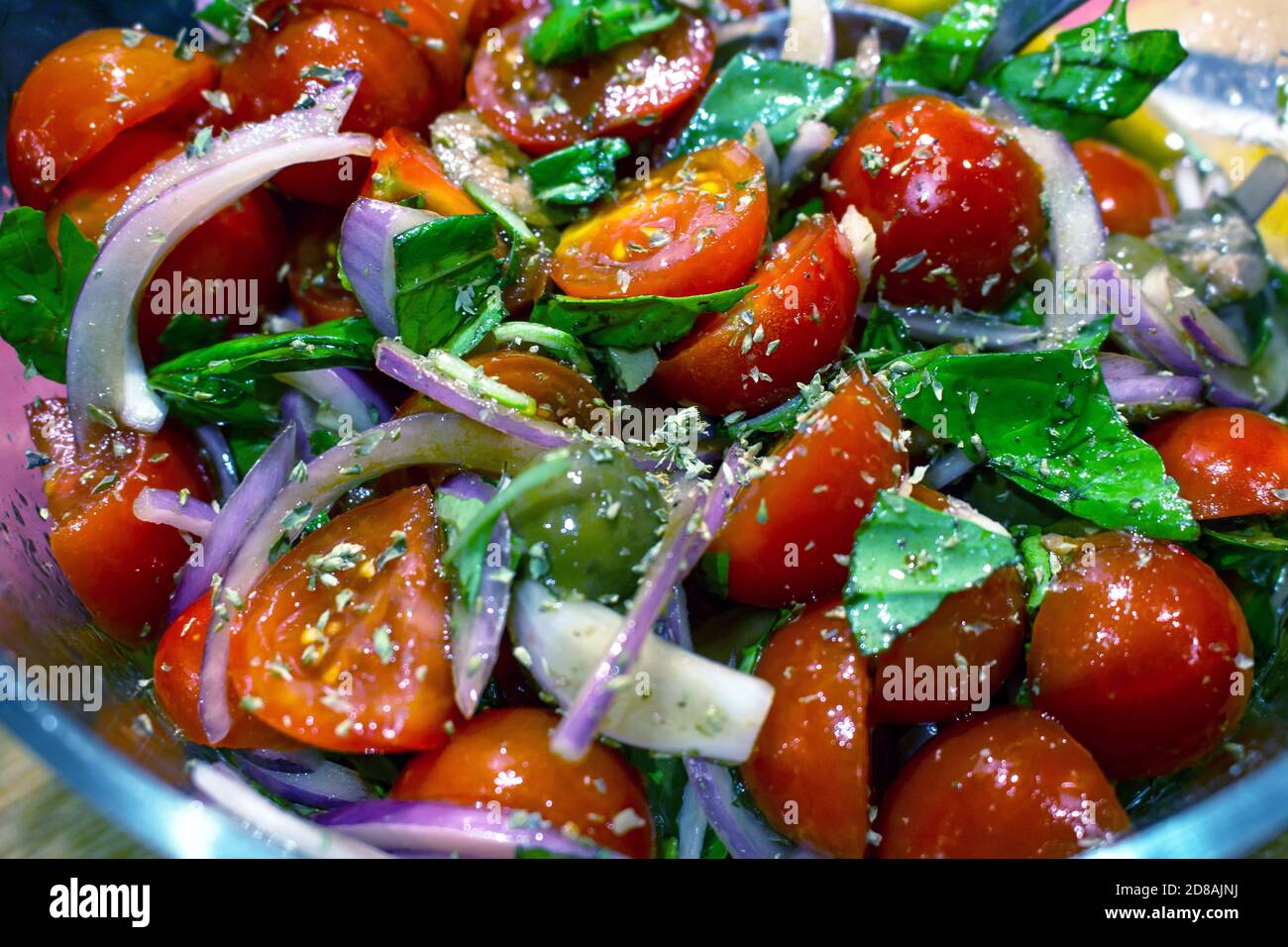 Una colorata insalata mediterranea con pomodori ciliegini, cipolla rossa di Tropea, basilico, origano e olive verdi Foto Stock