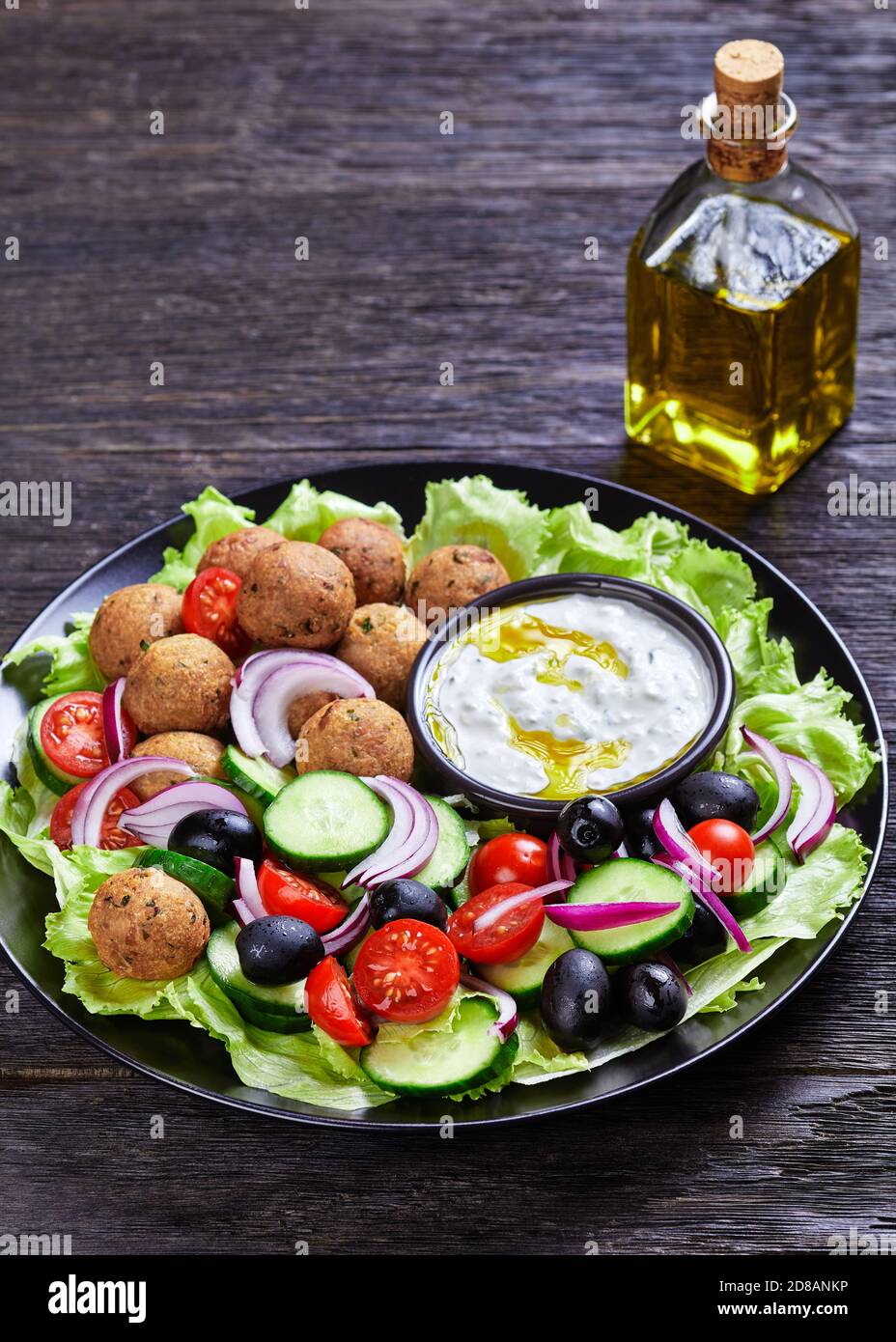 Piatto mediterraneo di falafel, pomodori, cetrioli, cipolla rossa, olive nere, sulle foglie fresche di insalata servite con salsa tzatziki servita su un nero Foto Stock