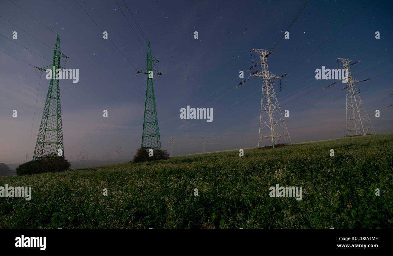 Torri di piloni elettrici ad alta tensione e linee di cavi di alimentazione di notte. Notte cielo stelle sfondo. Foto Stock