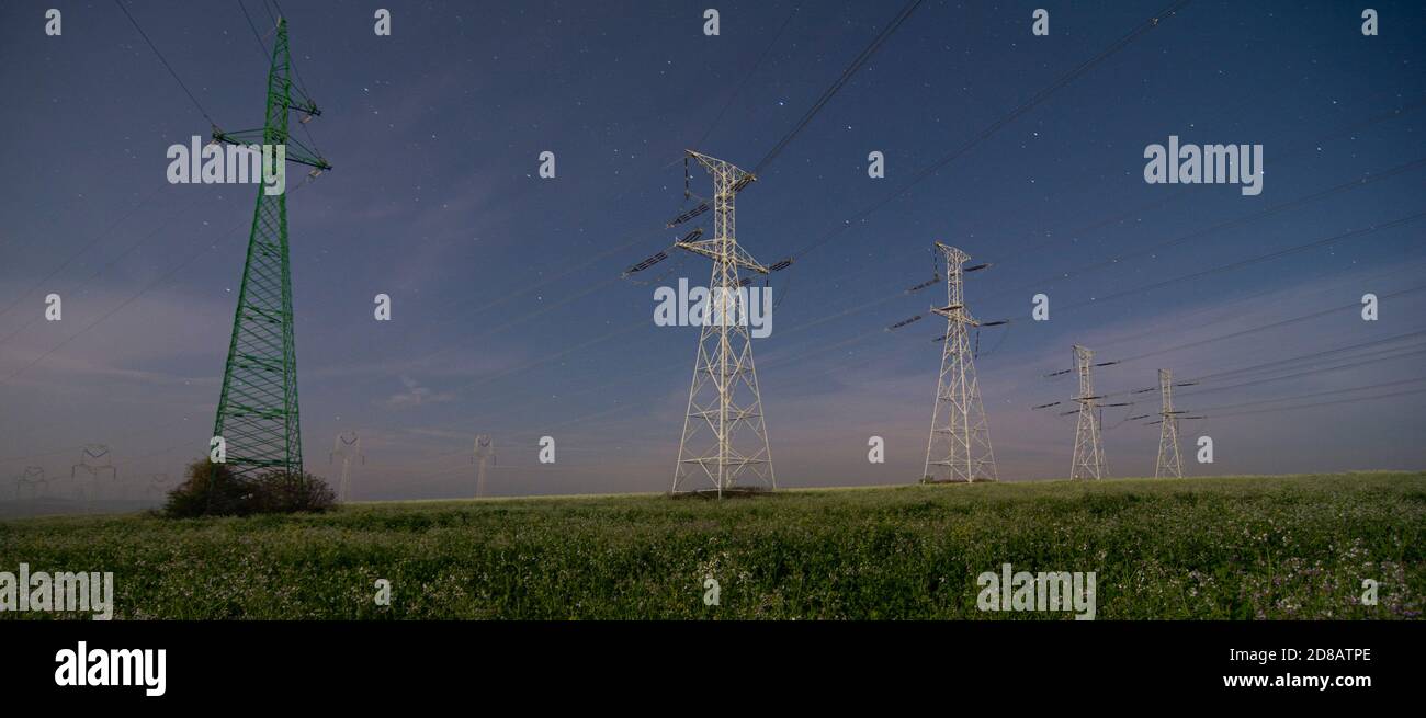 Torri di piloni elettrici ad alta tensione e linee di cavi di alimentazione di notte. Notte cielo stelle sfondo. Foto Stock