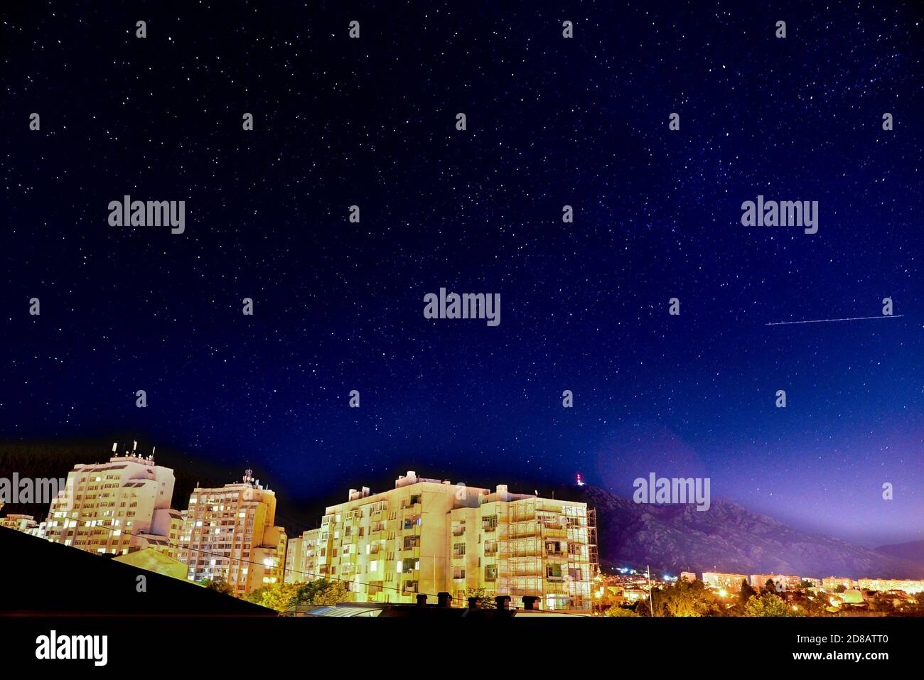 Stella cadente o un aereo dell'aria visibile in una stellata notte sopra un blocco di alloggiamento della città Foto Stock
