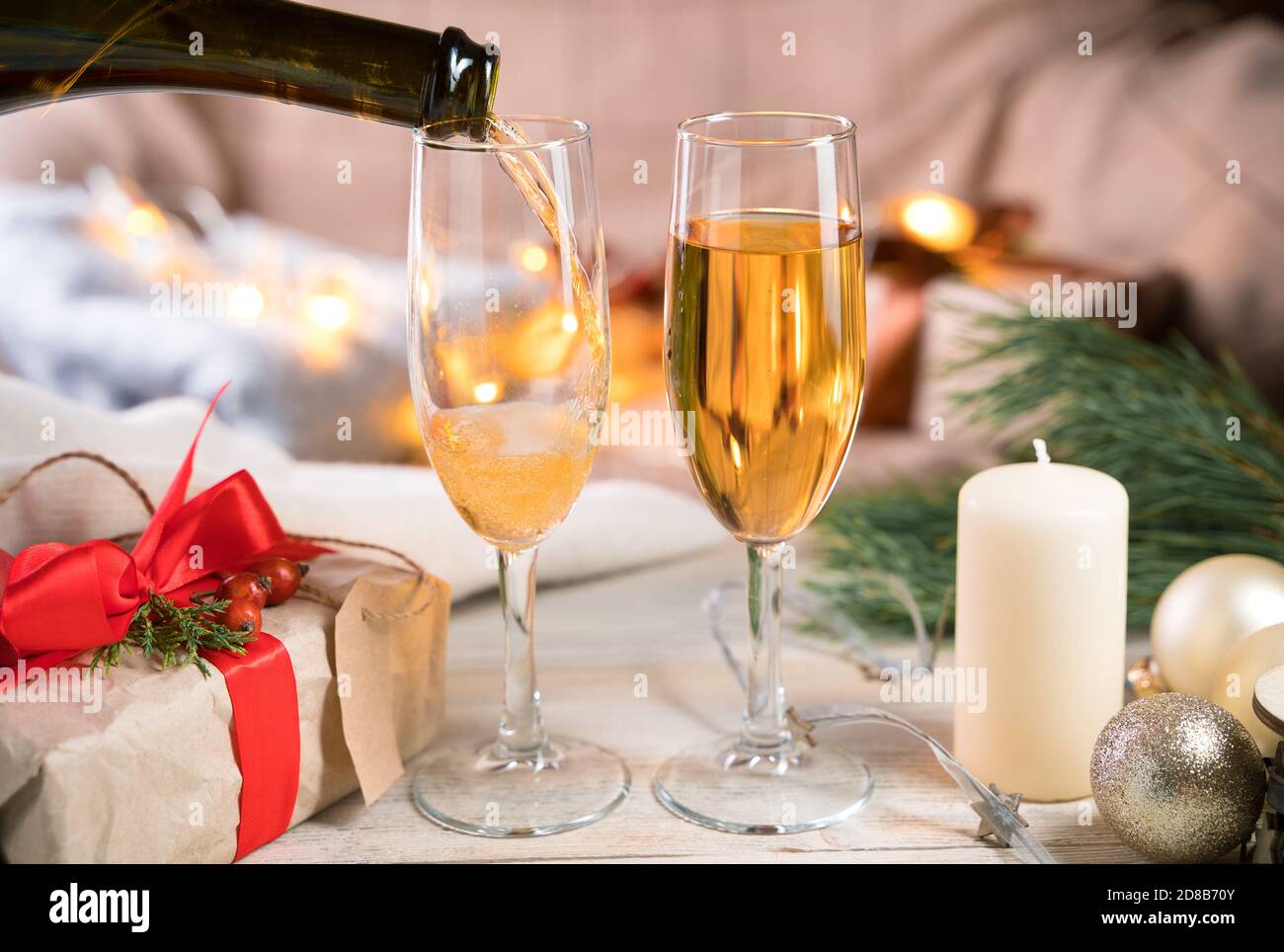 Due bicchieri e una bottiglia di champagne, il processo di versare champagne in bicchieri in camera in un'atmosfera accogliente. Foto Stock