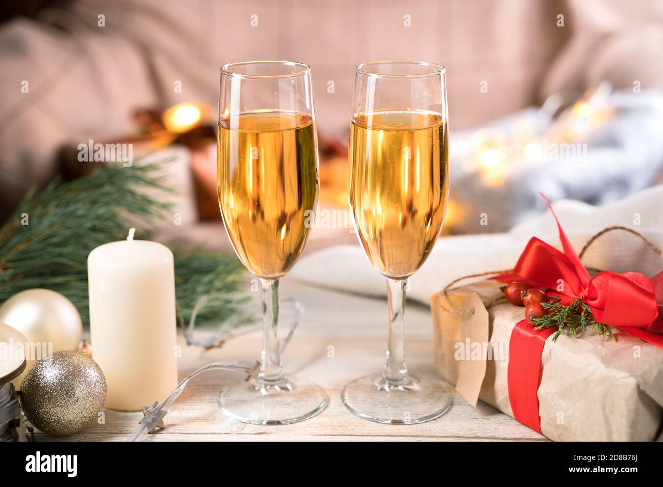 Due bicchieri di champagne, un regalo e una candela sul tavolo in un'atmosfera natalizia. Foto Stock