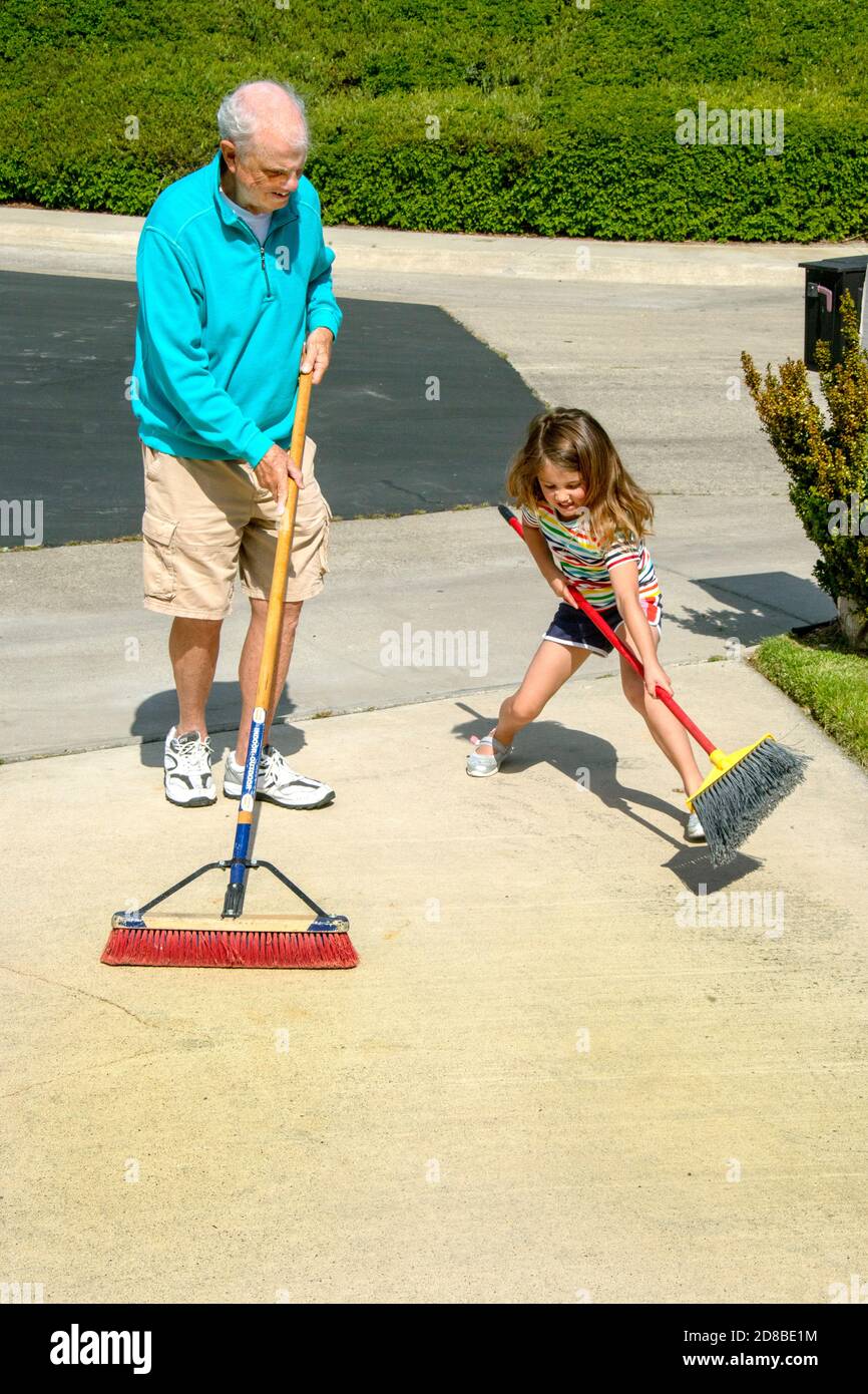 Un nonno e una nipote condividono un vialetto che spazza le faccende in una strada suburbana della California del Sud. Foto Stock