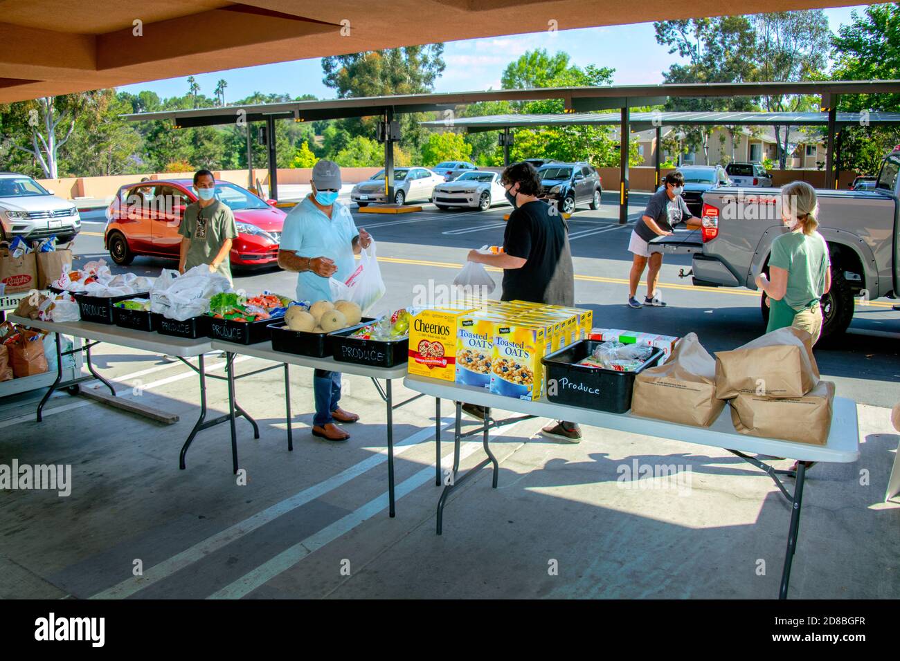 I volontari della dispensa alimentare di una chiesa cattolica della California meridionale distribuiscono generi alimentari per guidare attraverso i destinatari di beneficenza. Notare le maschere facciali dovute a. Foto Stock