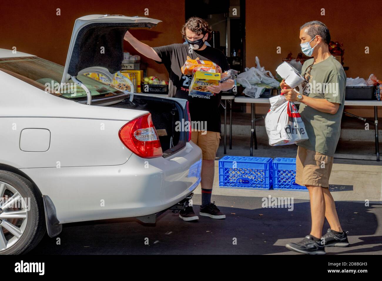 I volontari della dispensa alimentare di una chiesa cattolica della California meridionale distribuiscono generi alimentari per guidare attraverso i destinatari di beneficenza. Nota maschere facciali dovute Foto Stock