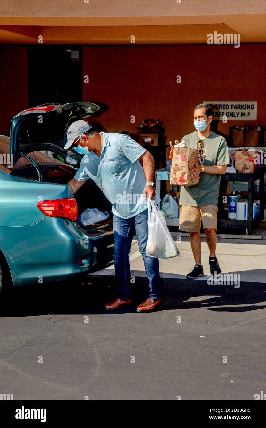 I volontari della dispensa alimentare di una chiesa cattolica della California meridionale distribuiscono generi alimentari per guidare attraverso i destinatari di beneficenza. Nota maschere facciali dovute Foto Stock