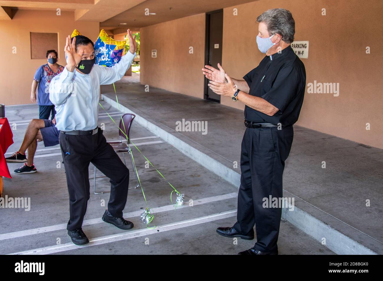 Un prete asiatico-americano in partenza fa una danza celebrativa mentre il suo monsignor si aggrappa ad una chiesa cattolica della California meridionale. Notare le maschere facciali dovute al decor Foto Stock