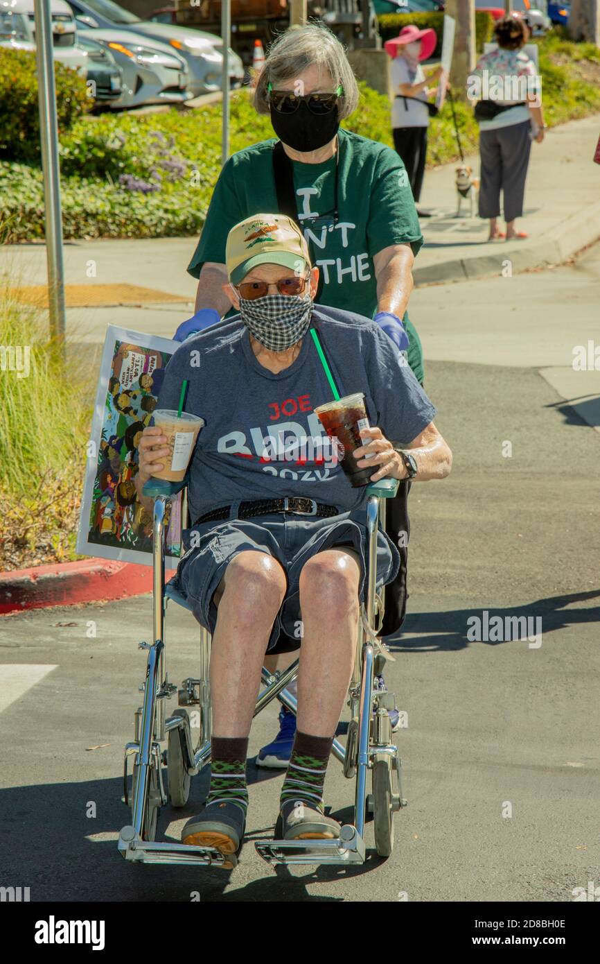 Un anziano sostenitore di Joseph Biden indossa un adeguato T-shirt come viene spinto nella sua sedia a rotelle a a. dimostrazione di suppo sul marciapiede Foto Stock