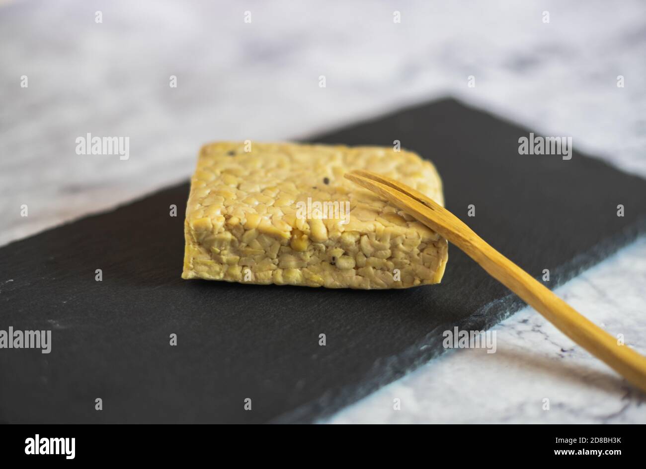 Pezzo di tempeh di soia su una tavola di ardesia su un piano di marmo con una forchetta di legno. Cibo asiatico sano. Foto Stock