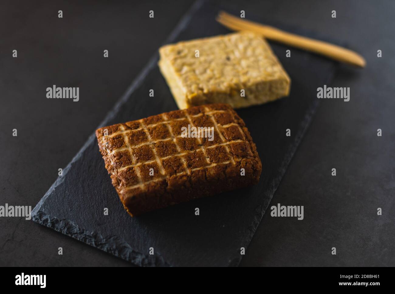 Due pezzi di prodotti di soia. Tofu affumicato e tempeh. Alimenti proteici sani su una tavola di ardesia Foto Stock Due pezzi di prodotti di soia. Tofu affumicato e tempeh. Alimenti proteici sani su una tavola di ardesia Foto Stock