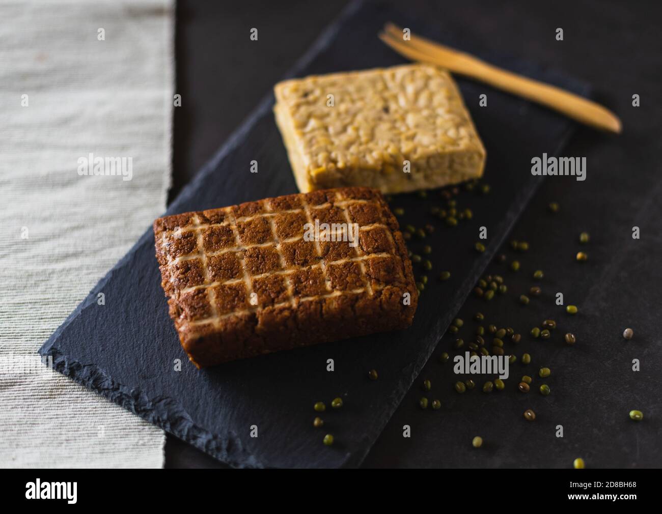 Due pezzi di prodotti di soia. Tofu affumicato e tempeh. Alimenti proteici sani su una tavola di ardesia Foto Stock Due pezzi di prodotti di soia. Tofu affumicato e tempeh. Alimenti proteici sani su una tavola di ardesia Foto Stock