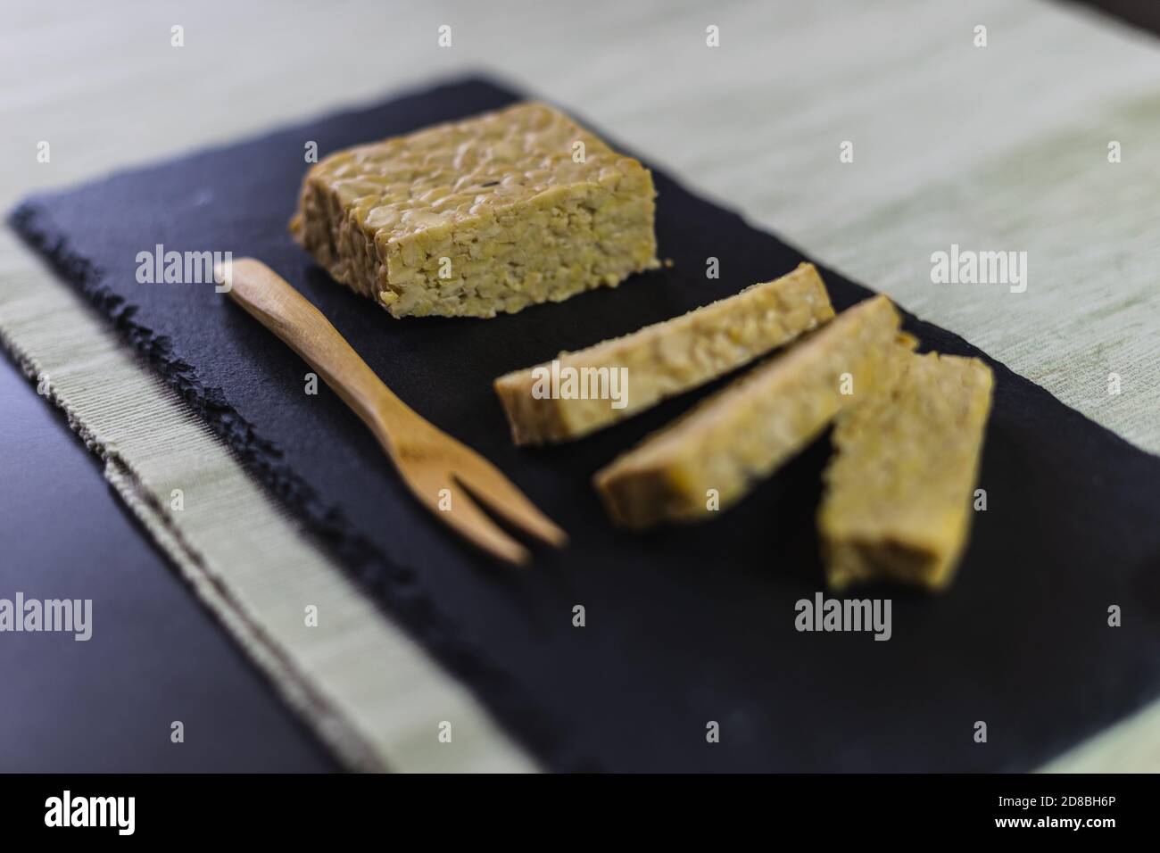 Un pezzo di nutriente tempeh di soia tagliato a fette su una piastra di ardesia e una forchetta di legno. Foto Stock