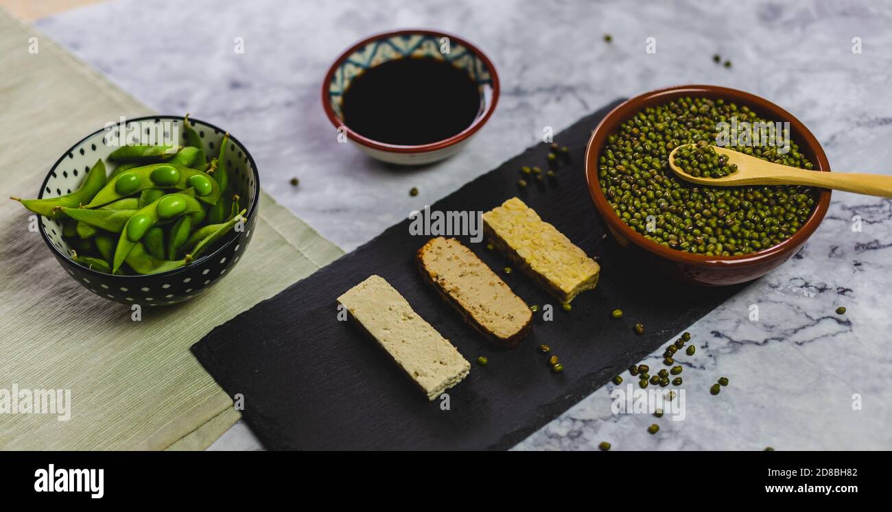 Prodotti diversi derivati dalla soia. Fagioli di edamame, salsa di soia, tofu, tempeh e soia. Cibo su una tovaglia su un piano di marmo. Foto Stock