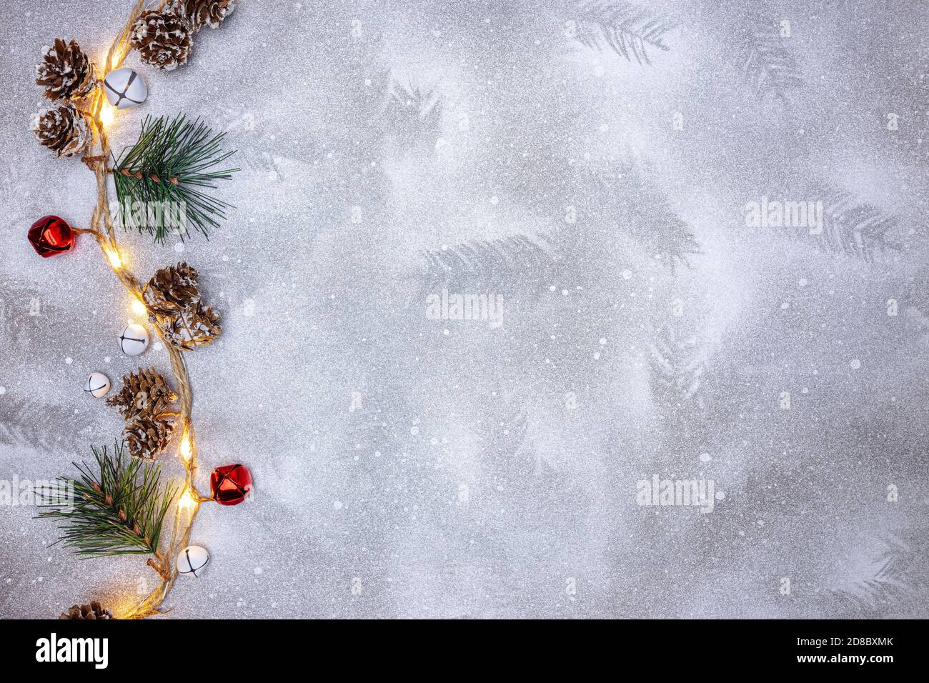 luci scintillanti garland decorato con coni di pino e campane di jingle su sfondo argento festivo Foto Stock