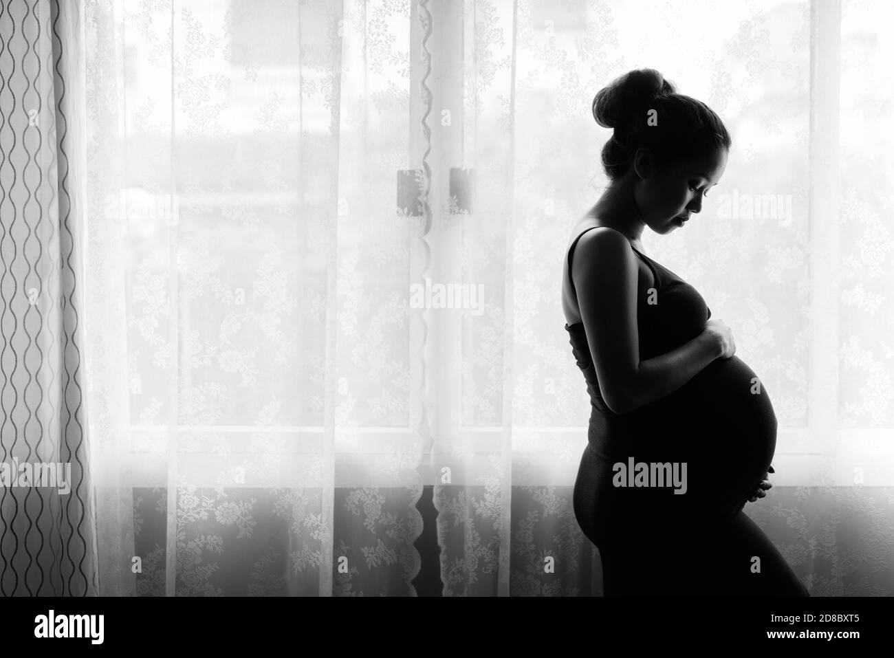 Madre di amare il suo bambino in silhouette mediante la finestra Foto Stock